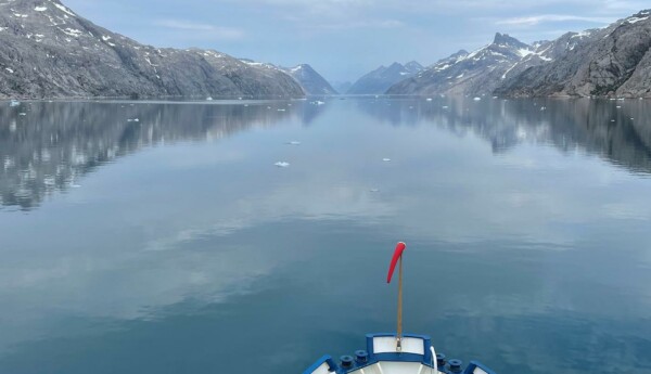 Fören på en båt som färdas i en fjord. Havsytan är glasblank.
