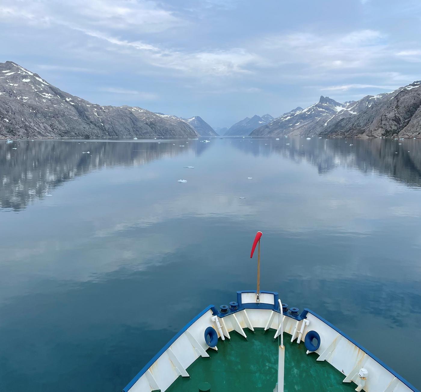 Fören på en båt som färdas i en fjord. Havsytan är glasblank.