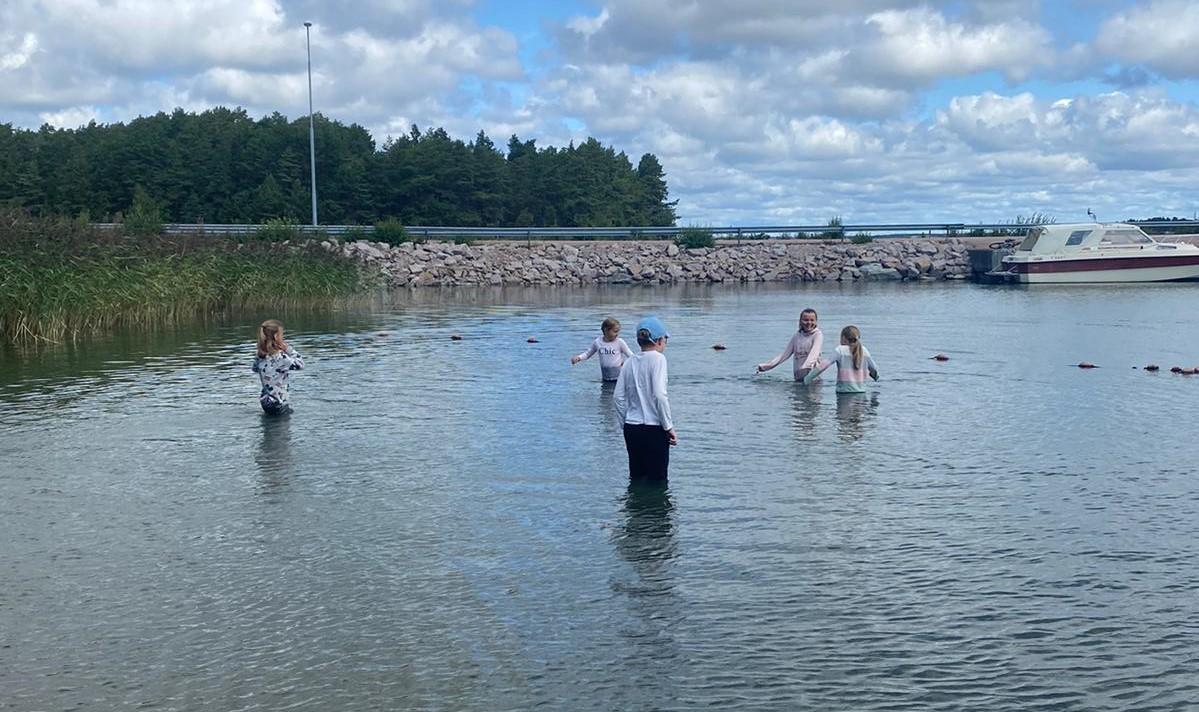 Barn står i vattnet med kläder på och ser ut att frysa.