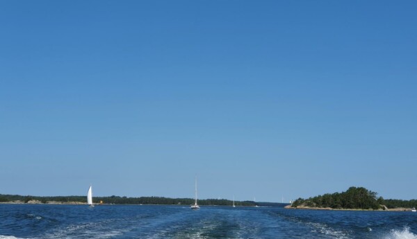 Några segelbåtar syns på avstånd i havet, lummig ö på håll.