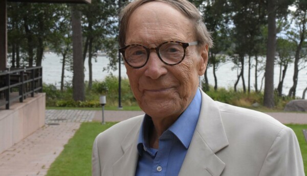 Man med glasögon och blå skjorta och ljus kavaj ler mot kameran