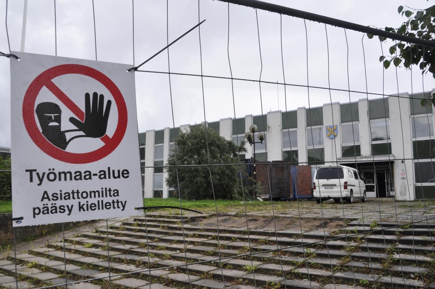 Staket och skylt om byggarbetsplats invid en låg byggnad
