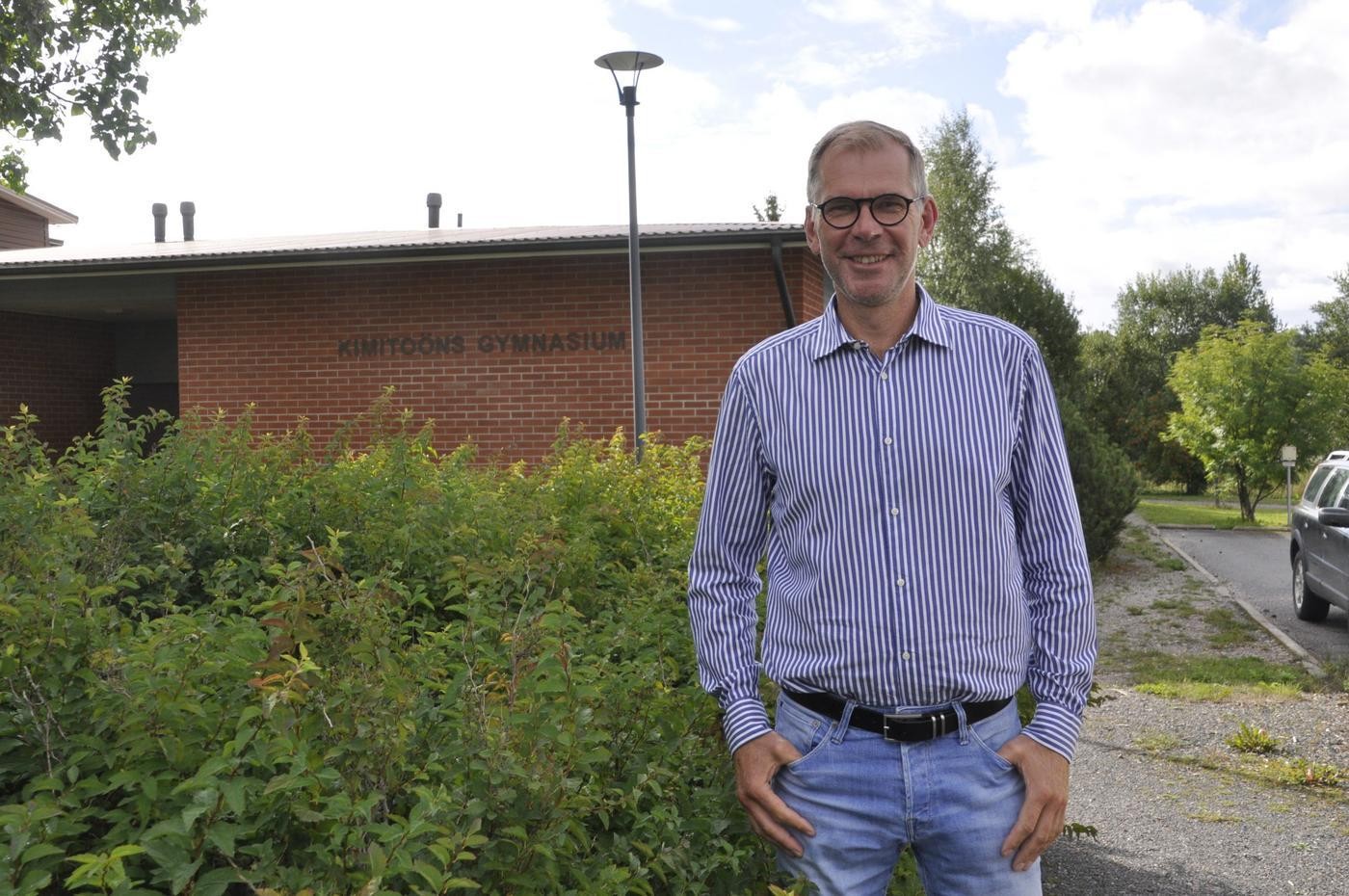 man vid tegelbyggnad med texten Kimitoöns gymnasium
