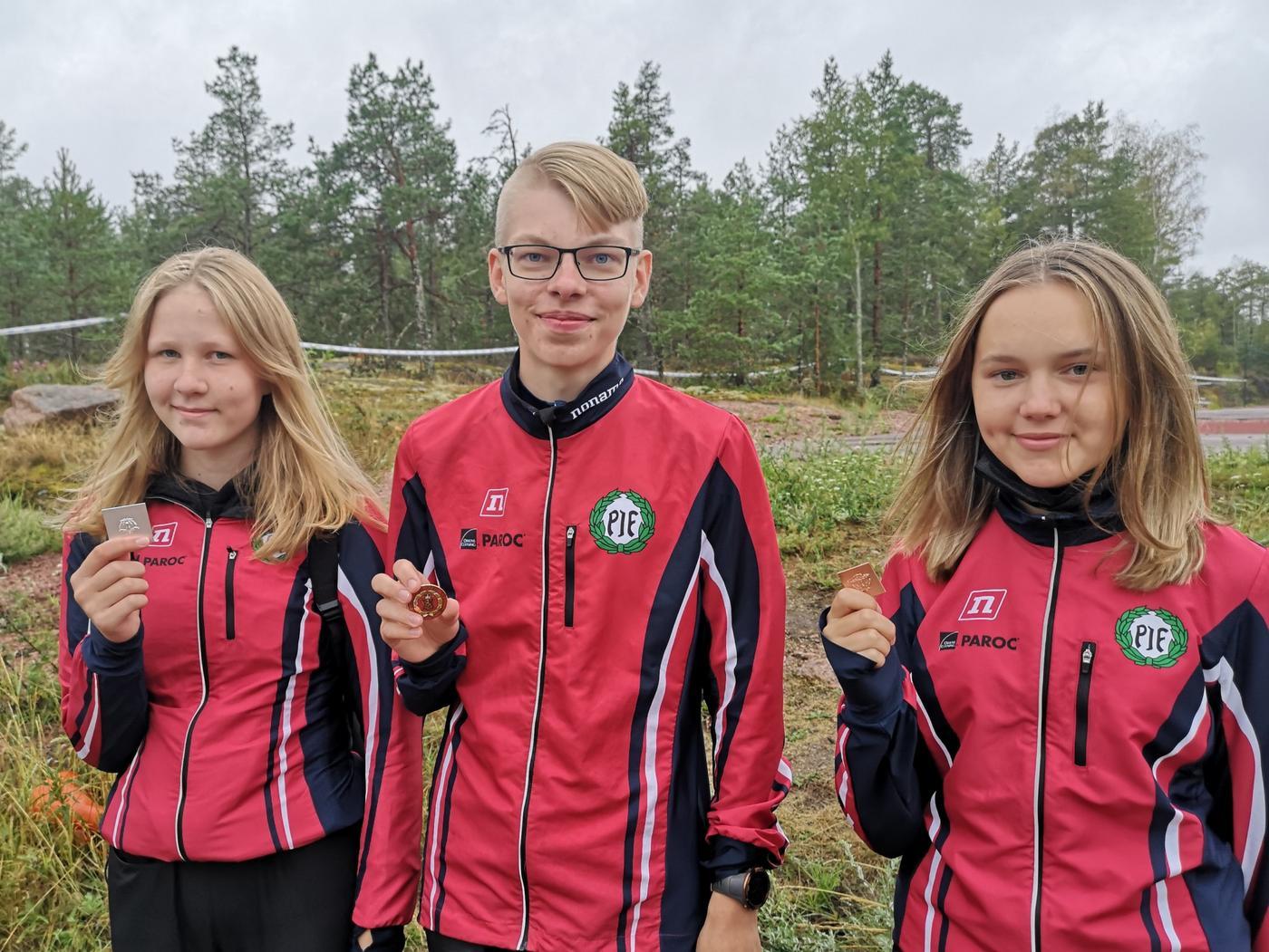 Tre ungdomar i röda föreningsdräkter håller upp medaljer.