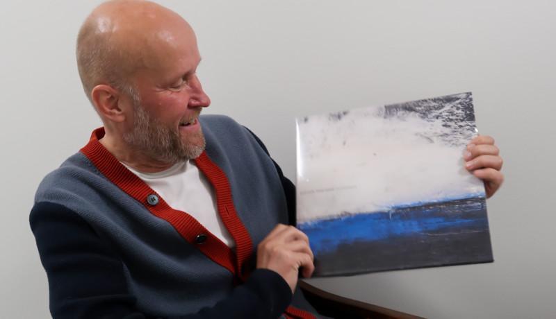 Porträtt av man som sitter och håller upp en vinylalbum som han tittar på. Albumets omslag föreställer en målning av ett hav.