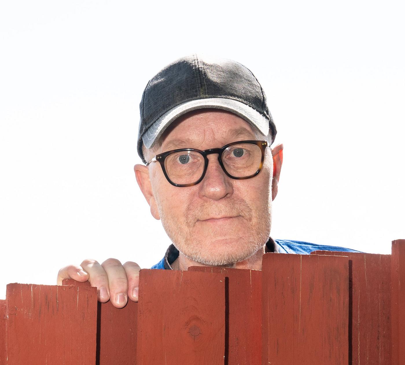man med glasögon och keps tittar fram bakåt ett staket