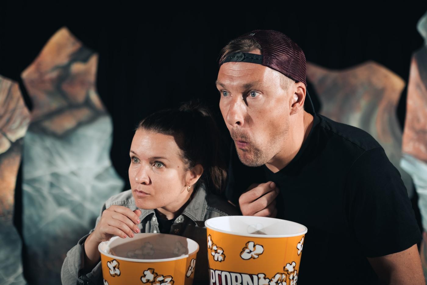 Outi Paasivirta och Mikael Strömberg i rollerna Lill och Olli i pjäsen "Stormen". De täer pocorn och ser gripet ut över publiken.