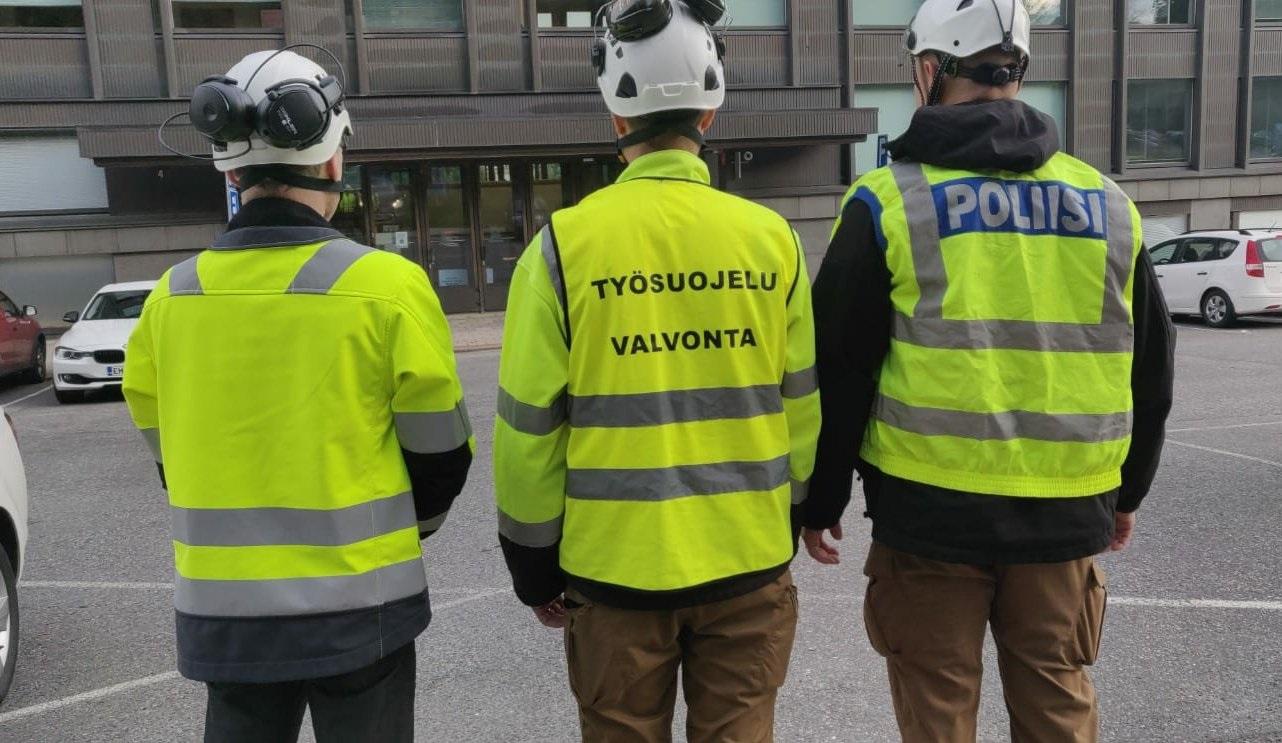 tre personer med reflexvästar på står med ryggarna mot kameran
