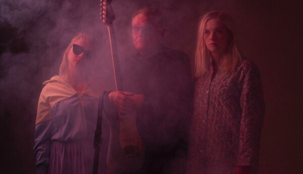 Två kvinnor och en man med gitarr poserar