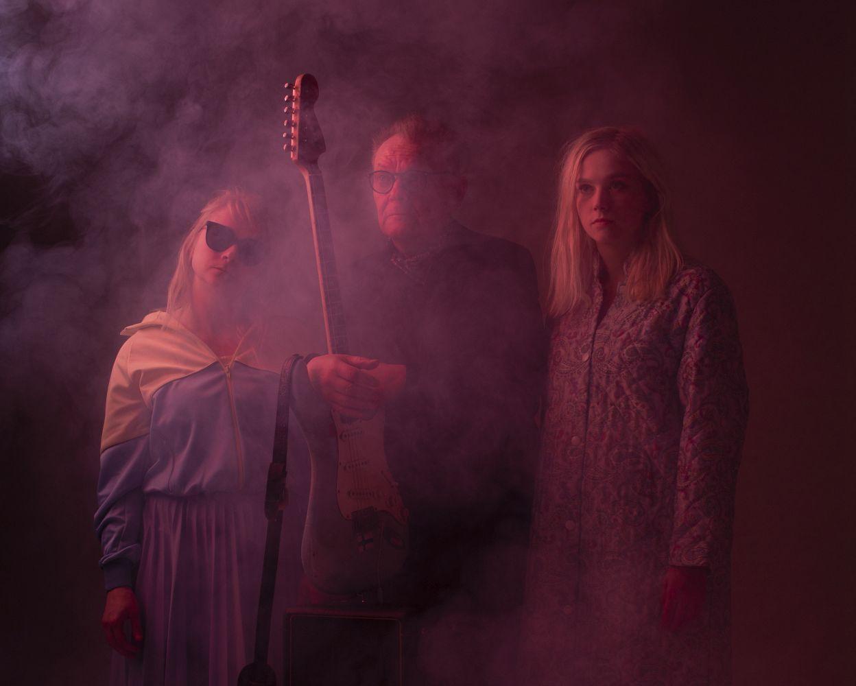 Två kvinnor och en man med gitarr poserar