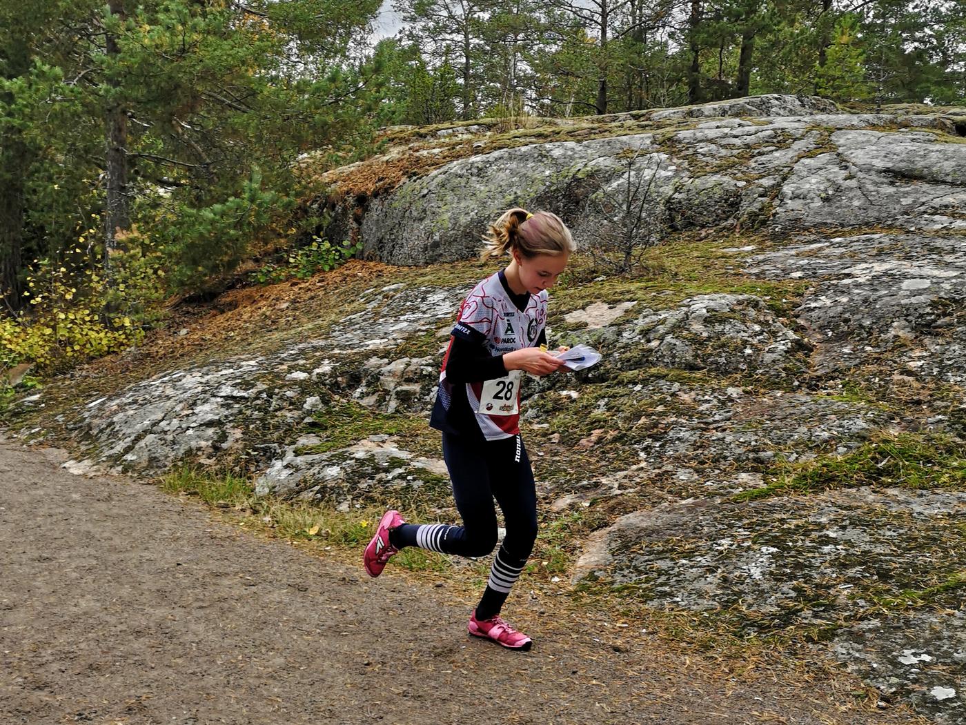 Flicka springer på grusväg vid en klippa.