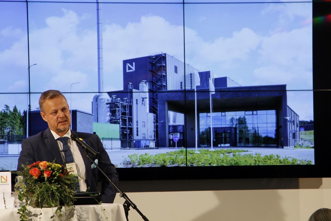 Man håller tal. Stor bild i bakgrunden av byggnad