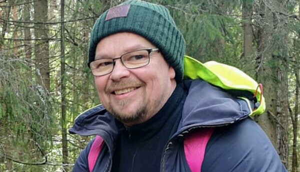 en man sitter med mössa på i skogen