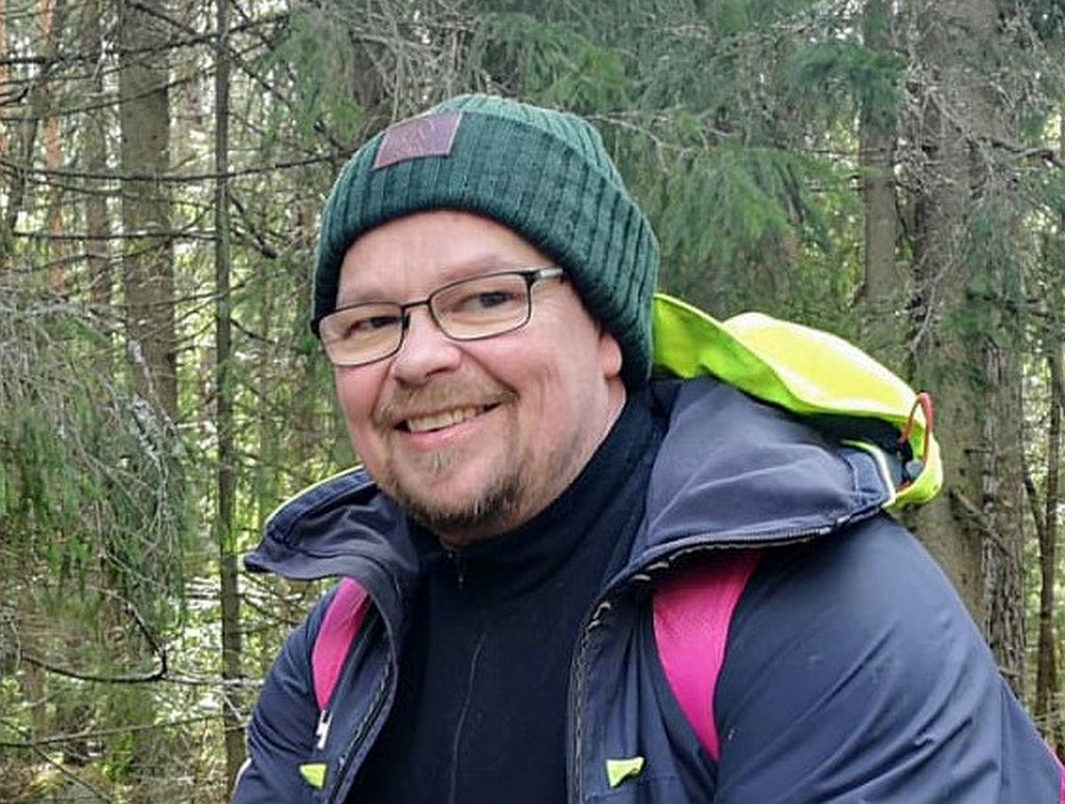 en man sitter med mössa på i skogen