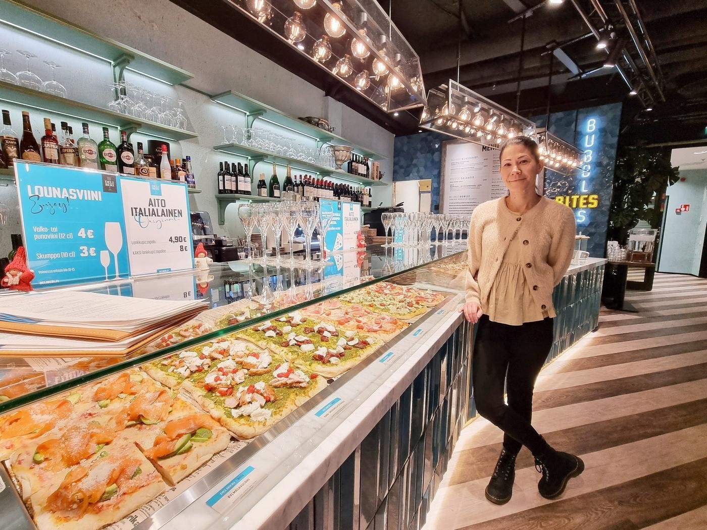 En kvinna som står bredvid en vitrin med pizza.