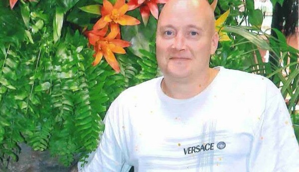 Skallig man i t-tröja står vid blomsterbuske