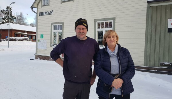 två personer utanför en träbyggnad