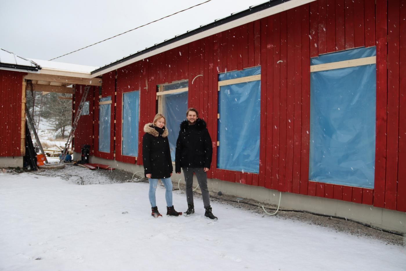 ett par framför en röd byggnad med blå byggplast för fönstren
