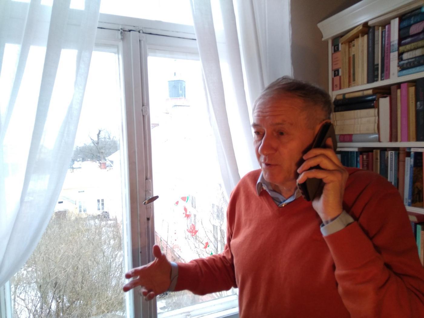 En man står och talar i telefon. Genom fönstret i bakgrunden skymtar Åbo Domkyrka.