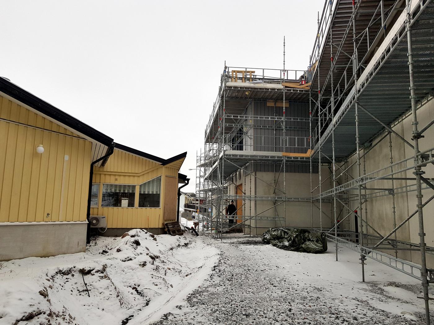 Gul äldre och mindre byggnad alldeles intill ett nybygge med byggnadsställningar