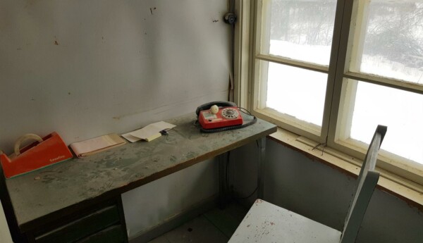 Dammigt gammalt skrivbord där det står en röd trådtelefon
