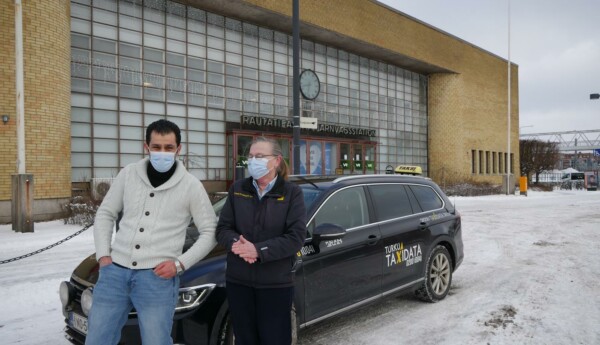 En man och en kvinna står vid en taxibil framför Åbo centralstation.