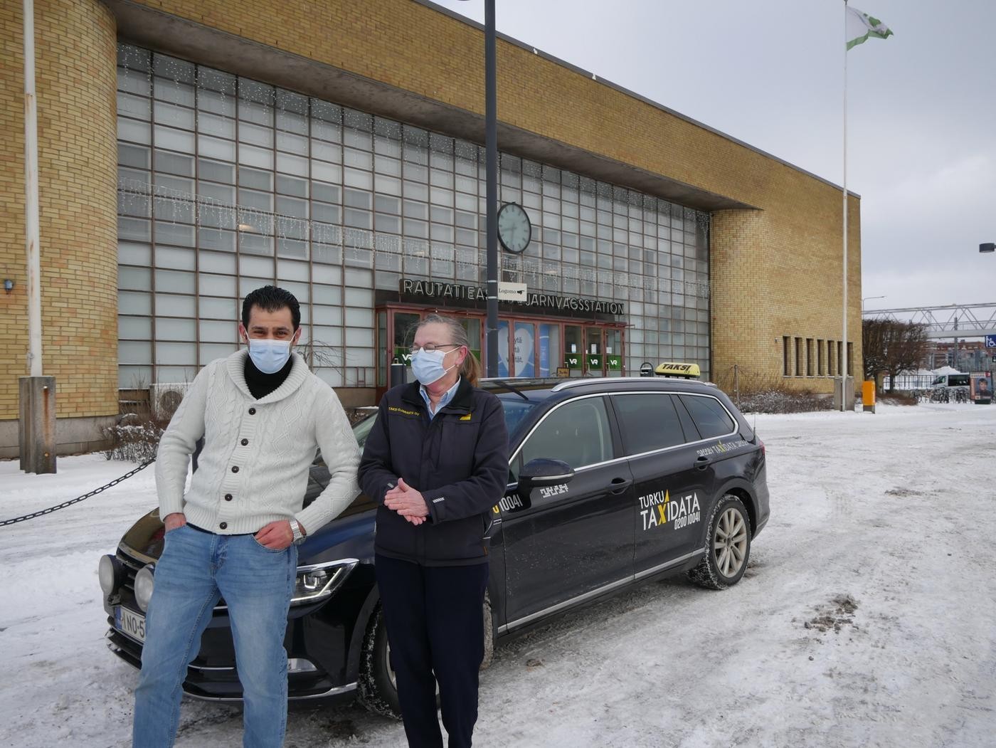 En man och en kvinna står vid en taxibil framför Åbo centralstation.