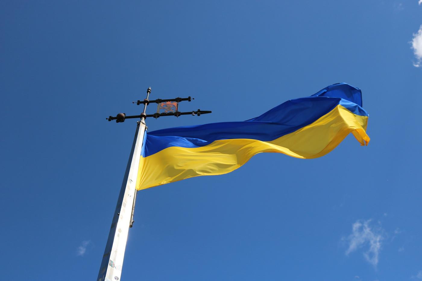 Blågul flagga vajar i vinden, upphissad i flaggstång.