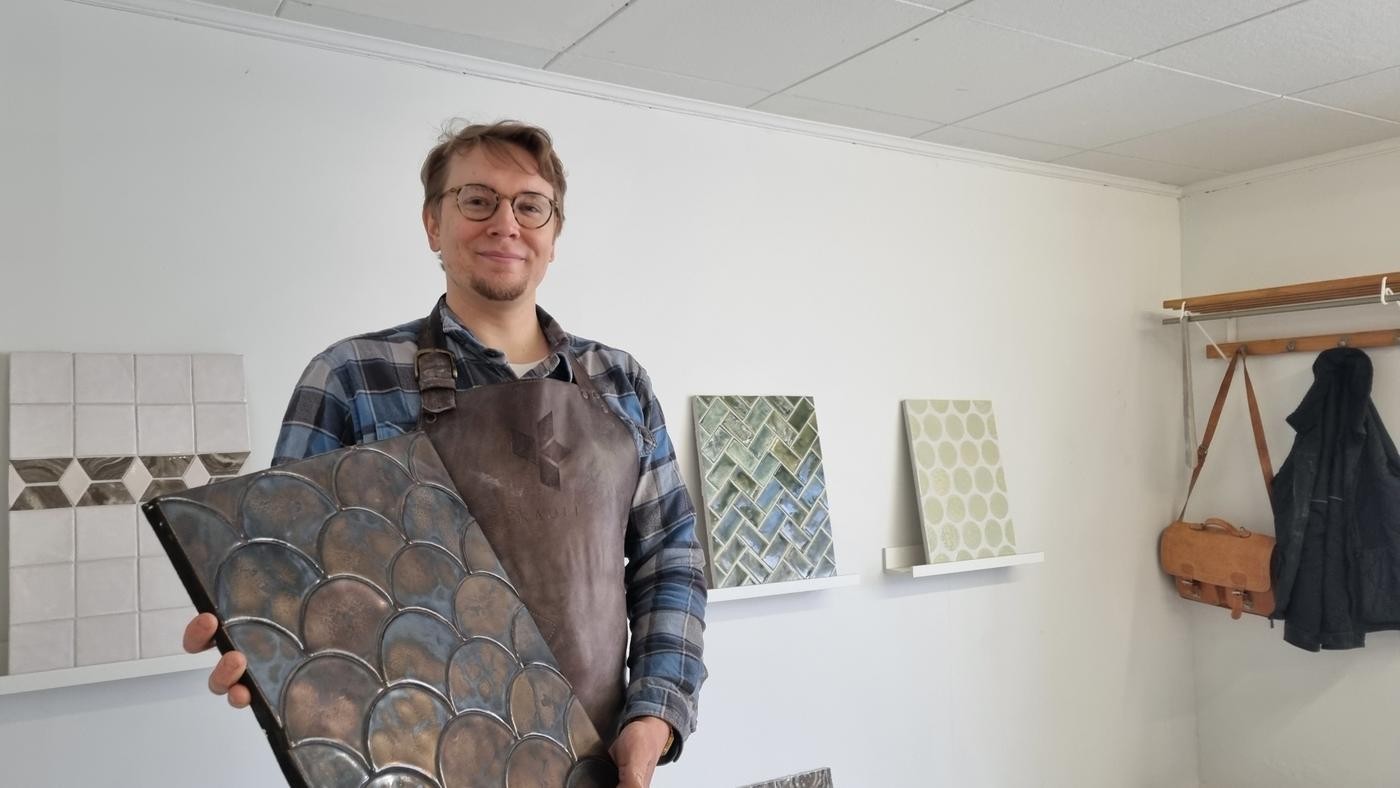 man visar upp skiva med handgjorda kakel