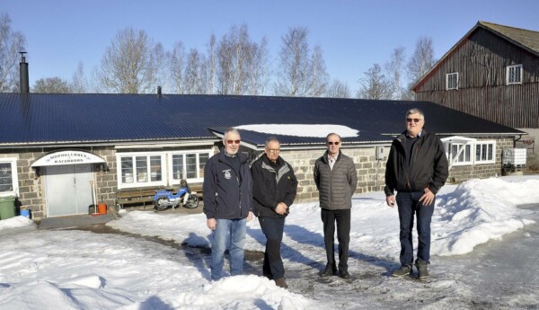 Fyra män framför en låg tegelbyggnad.