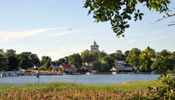 Sommar. En vik, trähus och ett kyrktorn