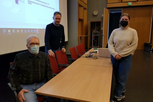 tre personer vid ett bord. En presentation på vita duken syns bakom.