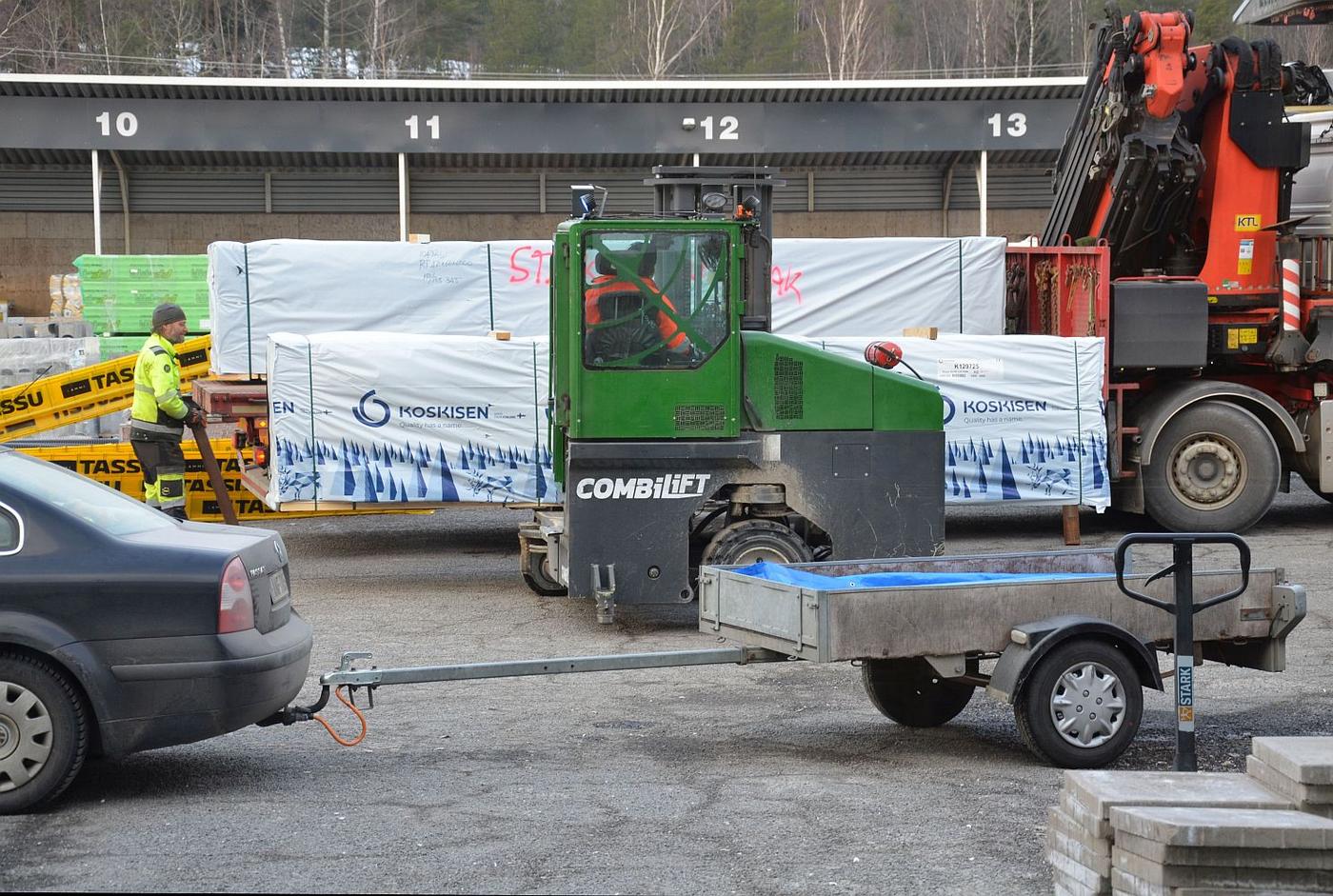 Arbetare, personbil med släpvagn, lastbil på byggvaruföretags gård.