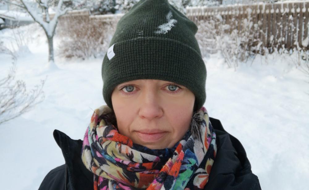 kvinna med mössa och snö i bakgrunden tittar in i kameran