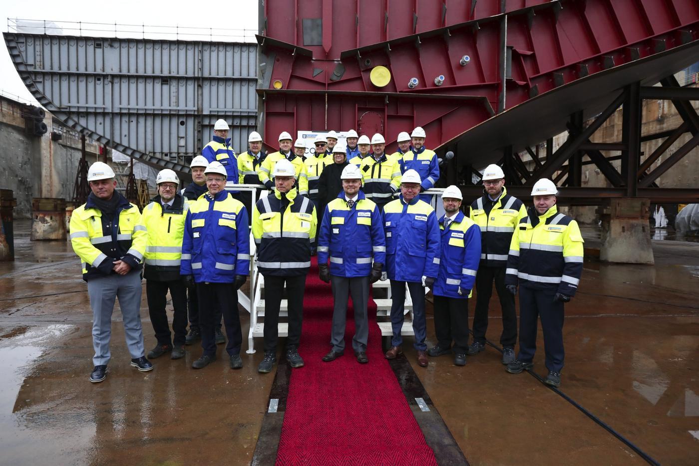 En grupp med mest män i arbetsjackor och hjälmar