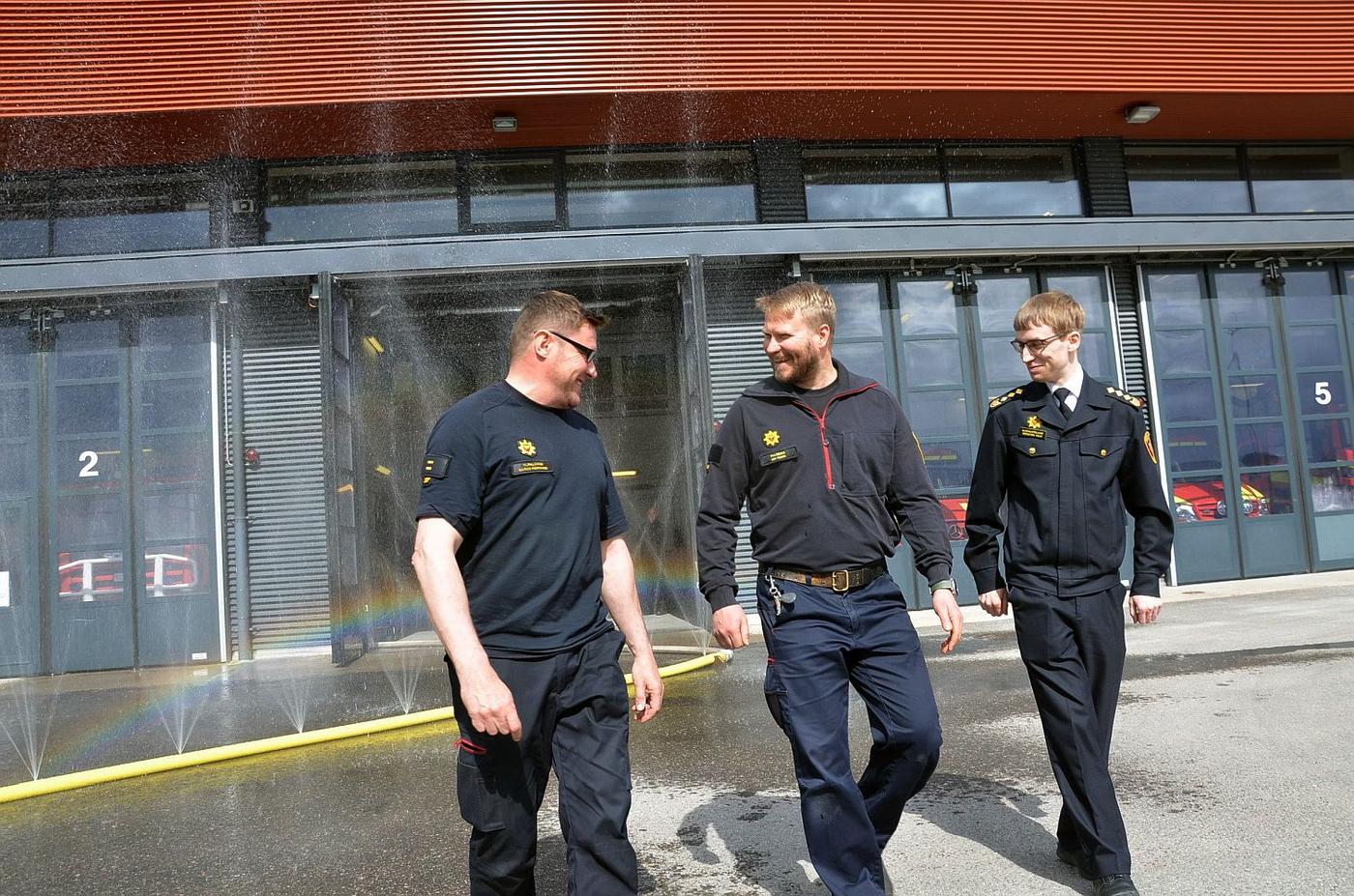 Tre brandmän övar med vattensprutande slang