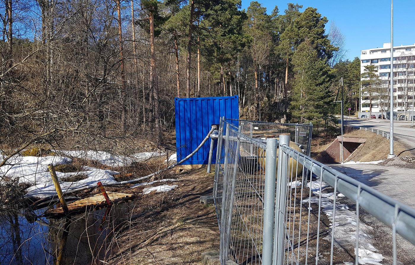 Vattenpöl, vattenrör, staket, container och höghus