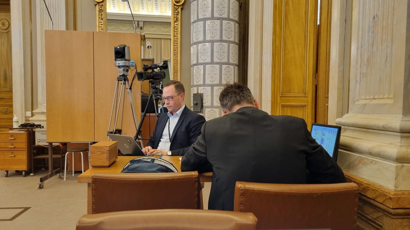 en man skriver på dator, annan man med mörk kostym sitter med ryggen mot kameran