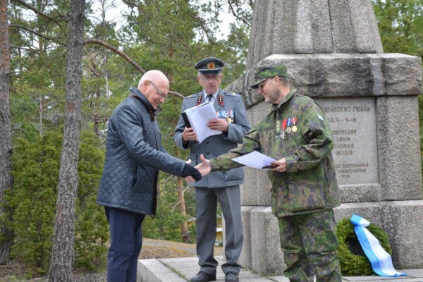 en man i grön militärklädsel skakar hand med en civilklädd man