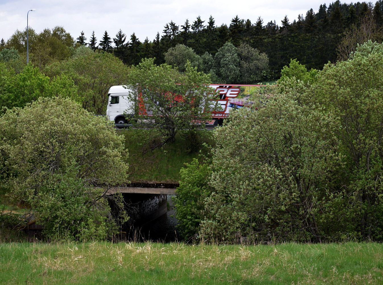 Långtradare kör över bro i lummig lantlig miljö