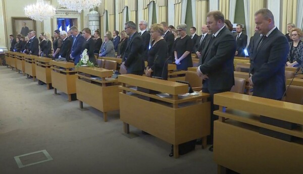 Sorgklädda politiker står under tyst minut i mötessalen
