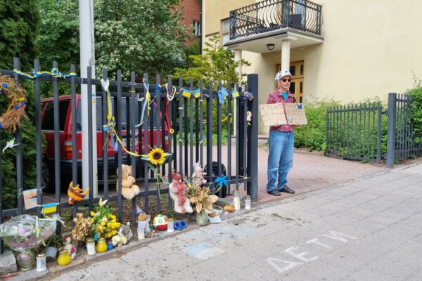 ensam kvinna demonstrerar vid staket med blommor och nallar