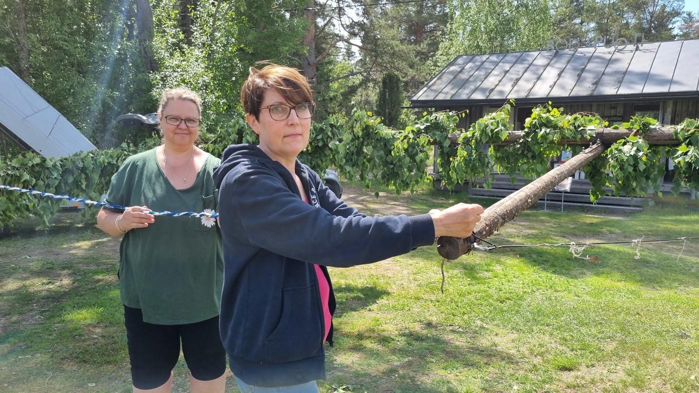 två kvinnor dekorerar en midsommarstång