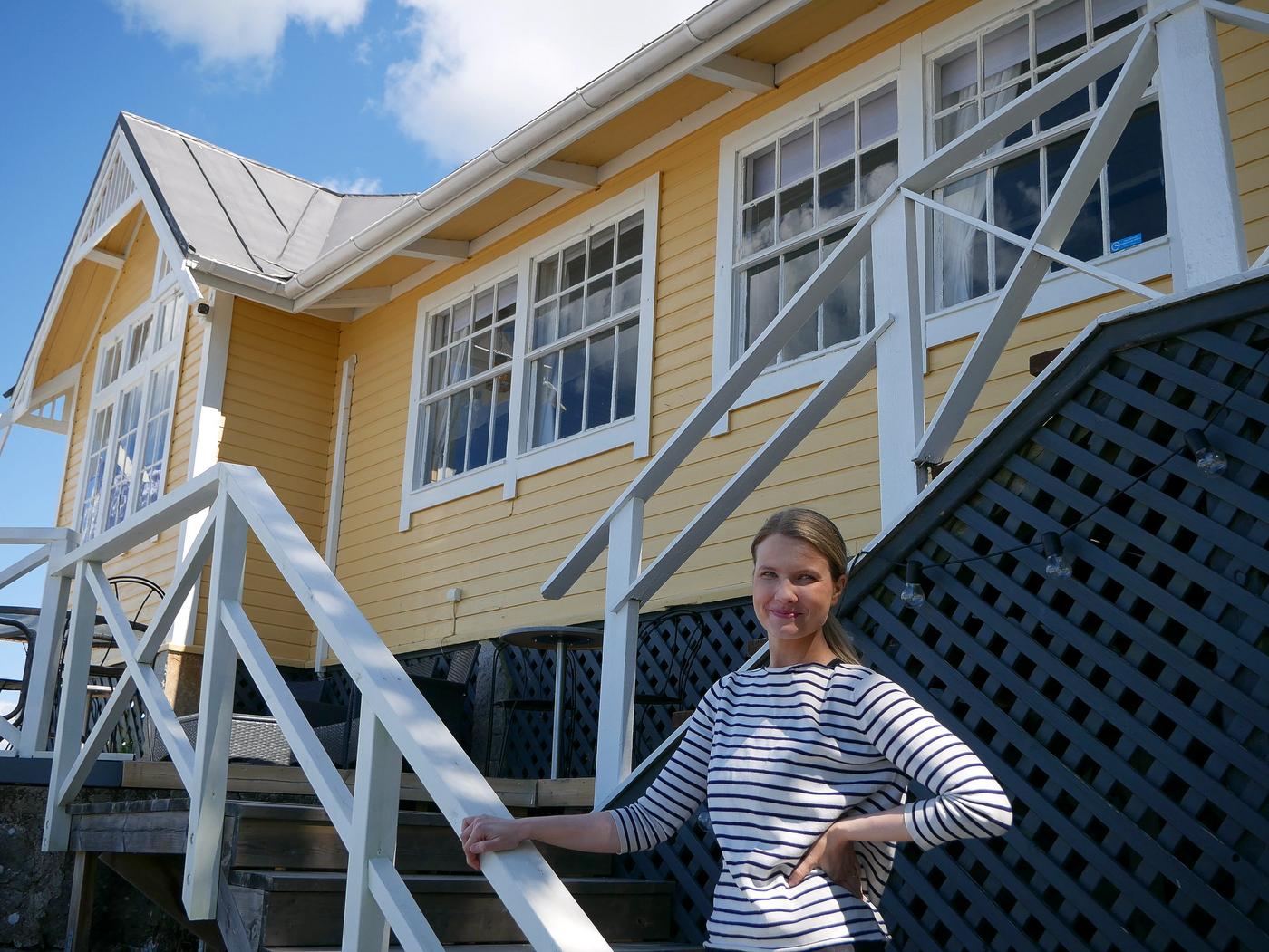 Kvinna står i trappan vid paviljong. Gult hus.