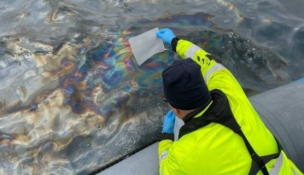 man i neongul jacka tar prov av olja i havsvatten