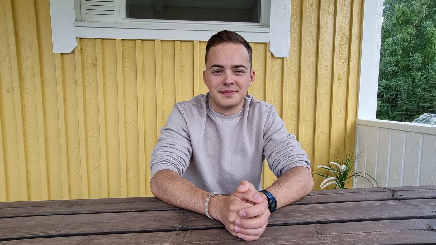 ung man sitter vid ett träbord framför gul brädvägg