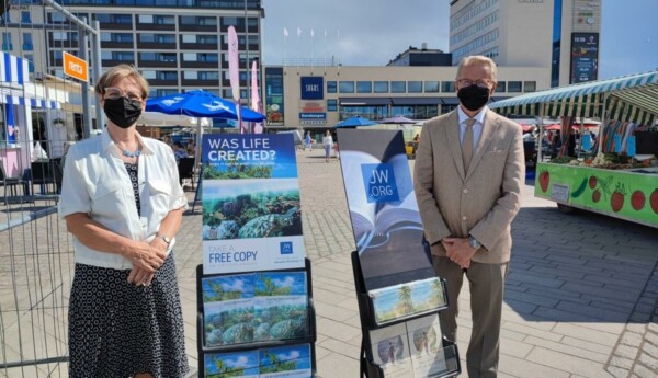 En kvinna och en man står på ett torg med flygblad om Jehovas vittnen.