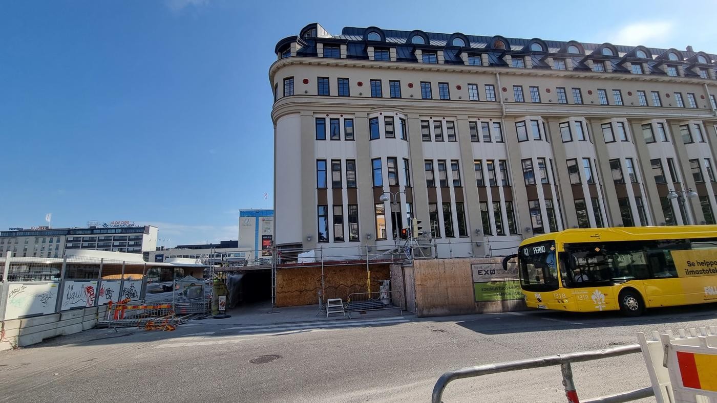 fasad på stor byggnad och gul buss till höger