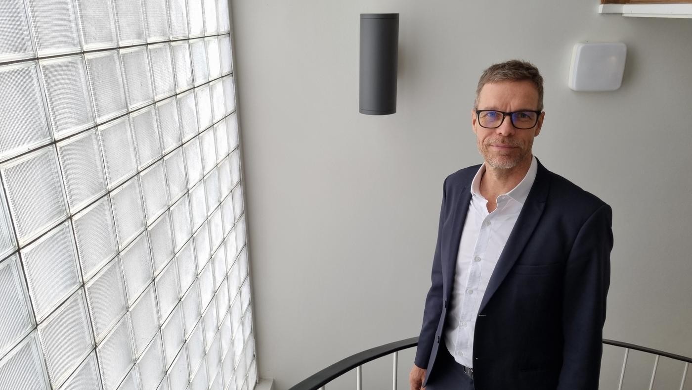 man med glasögon står vid vägg med små glasrutor