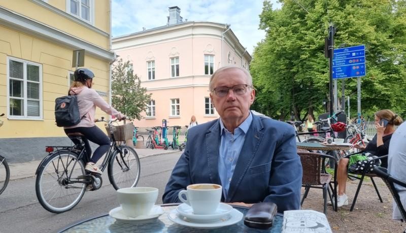 man med blå kavaj sitter vid cafébord utomhus